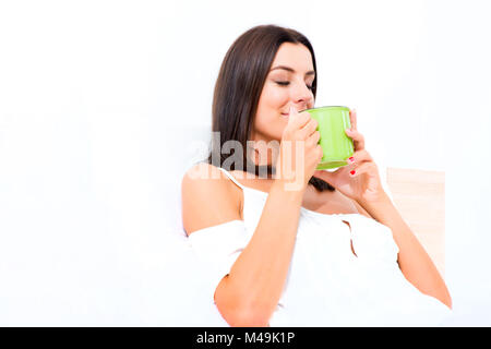 Schöne junge Frau, die ihren ersten Kaffee im Bett Stockfoto