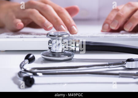 Nahaufnahme der Frau Hand Tippen mit Stethoskop auf Schreibtisch Stockfoto