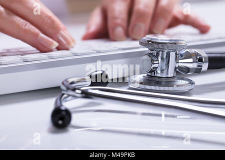 Nahaufnahme der Frau Hand Tippen mit Stethoskop auf Schreibtisch Stockfoto