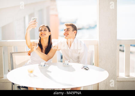 Attraktive Paar ersten Datum. Kaffee mit einem Freund. lächelnden Menschen glücklich machen eine selfie mit einem Smartphone. Sharing auf Social Media. Stockfoto