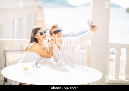 Attraktive Paar ersten Datum. Kaffee mit einem Freund. lächelnden Menschen glücklich machen eine selfie mit einem Smartphone. Sharing auf Social Media. Stockfoto