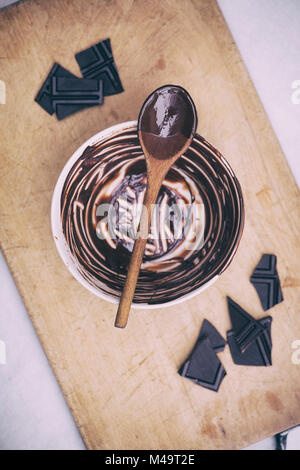 Geschmolzene dunkle Schokolade und Löffel aus Holz auf einem keramischen Rührschüssel. Vintage Filter angewendet Stockfoto