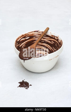Geschmolzene dunkle Schokolade und Löffel aus Holz auf einem keramischen Schüssel Stockfoto