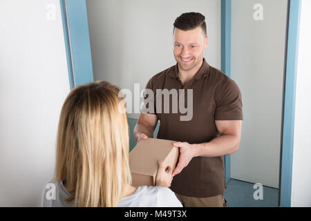 Glückliche junge Frau annehmen Paket Box von Delivery Man Stockfoto