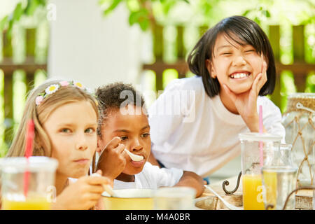 Kinder im internationalen Kindergarten frühstücken zusammen im Garten Stockfoto