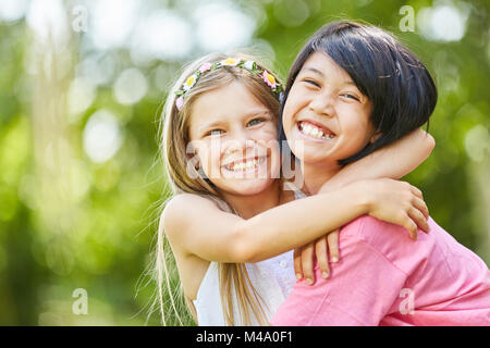 Zwei Mädchen als Freundinnen umarmen sich glücklich im Sommer im Park Stockfoto