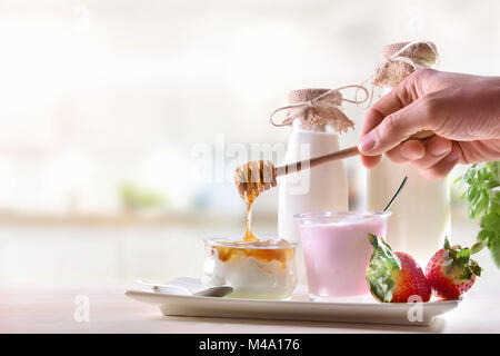 Molkerei in weißen Küche und hand Honig in Topfen mit Erdbeer Joghurt, Obst und Flaschen Milch Vorderansicht. Horizontale Zusammensetzung Stockfoto