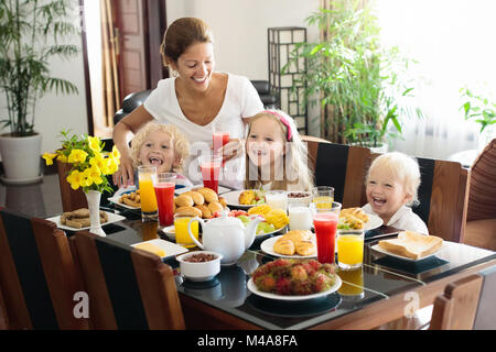 Gesunde Familie Frühstück zu Hause. Mutter und Kinder essen, tropische Obst, Toast, Brot, Käse und Wurst. Kinder trinken frisch gepressten Saft an sonnigen Stockfoto