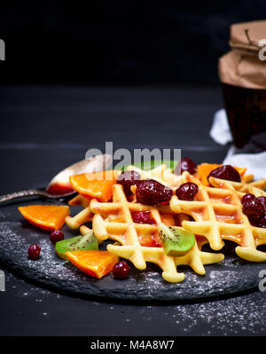Gebackene Belgische Waffeln mit Marmelade und frische Früchte auf einem schwarzen Hintergrund, in der Nähe Stockfoto