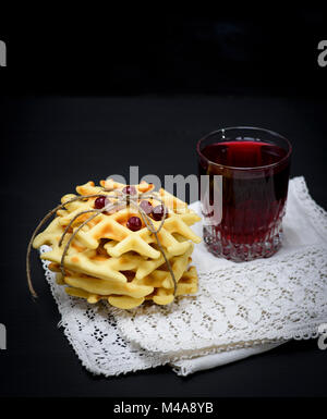 Gebackene belgische Waffeln und Kompott in einem Glas auf schwarzem Hintergrund Stockfoto