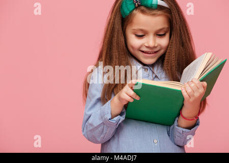 Close up Portrait von schönen Schulmädchen mit langen braunen Haaren lesen interessantes Buch, in glückliche Gefühle über rosa Hintergrund isoliert Stockfoto