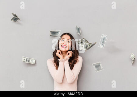 Bild von Lucky brünette Frau, sein aufgeregt Preisgeld unter Geld regen Spaß mit der Bar stehend über graue Wand zu gewinnen. Stockfoto