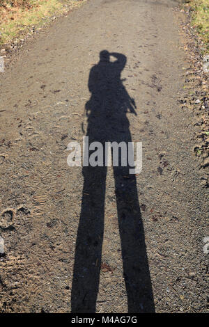 Schatten des Fotografen werfen auf einem Waldweg an einem sonnigen Tag. Stockfoto