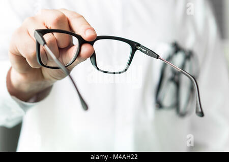 Optiker eine neue Brille zu Kunden für das Testen und Ausprobieren. Auge Arzt zeigt Patienten Objektive. Professionelle Optometriker in weißen Mantel.