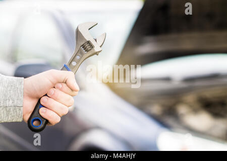 Auto Reparatur, Wartung und Inspektion Konzept. Mann mit Schraubenschlüssel vor einem Auto mit unter der Haube und Motor. Stockfoto