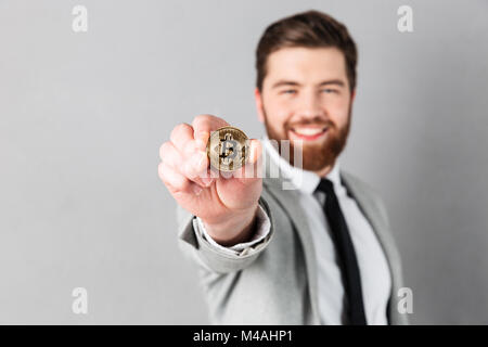 Nahaufnahme, Porträt eines lächelnden Geschäftsmann in Anzug gekleidet, bitcoin isoliert über grauer Hintergrund Stockfoto