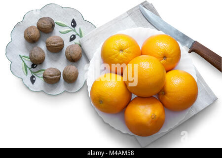 Orangen in der Schüssel und Walnüsse auf einem weißen Hintergrund. Stockfoto
