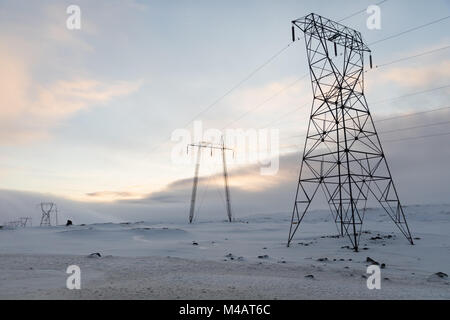 Hohe Hochspannungsleitungen in einer verschneiten Landschaft Stockfoto