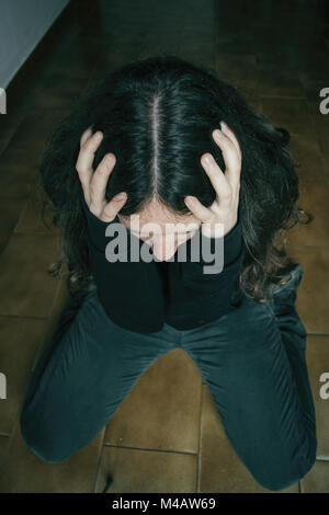 Trauriges Mädchen mit langen Haaren kniend auf dem Boden mit den Händen auf den Kopf Stockfoto