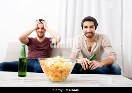 Zwei Freunde, die leidenschaftlich Fernsehen mit Bier und Chips Stockfoto
