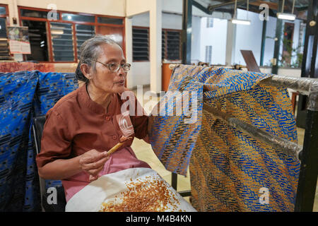 Die indonesische Frau trägt geschmolzenes Wachs auf Batik mit einem Canting (gegossenes Werkzeug) auf. Batik Winotosastro Shop, Yogyakarta, Java, Indonesien. Stockfoto