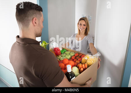 Lächelnden jungen Frau akzeptieren Karton voller Lebensmittel aus Delivery Man Stockfoto