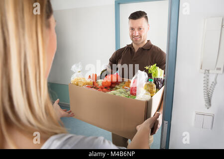 Lächelnden jungen Frau akzeptieren Karton voller Lebensmittel aus Delivery Man Stockfoto