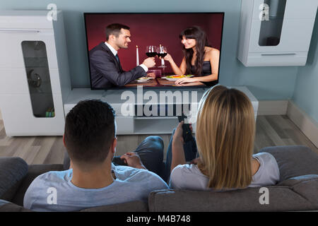 In der Nähe von ein paar Beobachten Paar beim Trinken zu Hause im Fernsehen Stockfoto