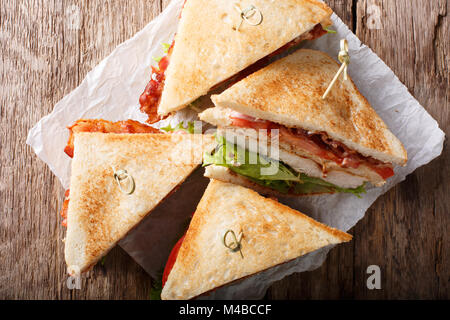 Layer Club Sandwich mit der Türkei Fleisch, Speck, Tomaten und Kopfsalat Makro auf Papier. Horizontal oben Ansicht von oben Stockfoto