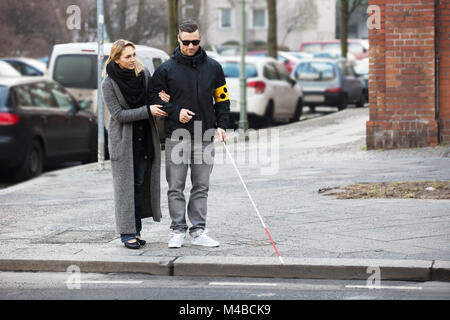 Junge Frau die Unterstützung blinder Mann mit weißem Stick auf der Straße Stockfoto