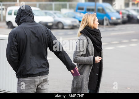 Mann in einer Haube Diebstahl Geldbörse aus der Frau Jackentasche auf der Straße Stockfoto