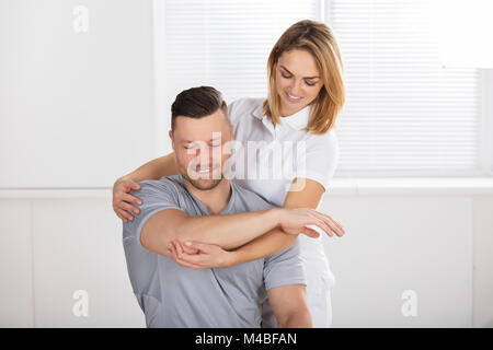 Junge lächelnde Frau Physiotherapeutin geben einen Mann schulter übung an der Klinik Stockfoto