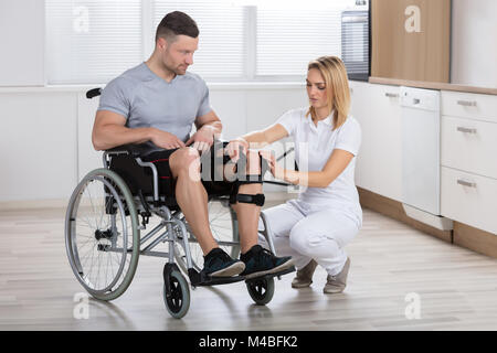 Junge weibliche Physiotherapeutin zur Festsetzung Knie Klammern auf der Man Bein in einer Klinik Stockfoto