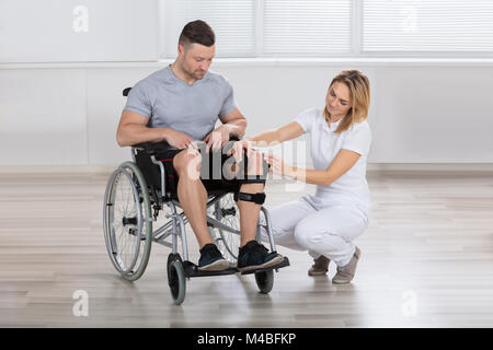 Junge weibliche Physiotherapeutin zur Festsetzung Knie Klammern auf der Man Bein in einer Klinik Stockfoto