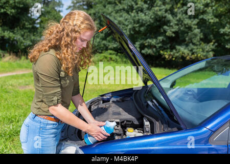 Niederländische Mädchen füllen Auto Behälter mit Flüssigkeit in der Flasche Stockfoto