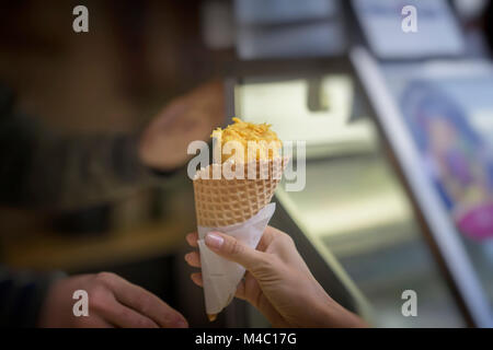 Leckeres Obst Eis ist neue Behandlung des Sommers. Kegel mit gelben Eis, hit neuer Geschmack, zwei Hände sind im Sommer vergnügen gezogen. Hintergrund Kopie Raum Stockfoto