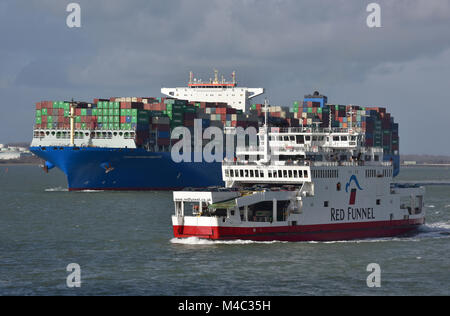 Die rote Insel von Wight Autofähre Trichter über den Solent in Southampton Docks oder Wasser vorbei an der riesigen Containerschiff costco Versand Himalaya. Stockfoto