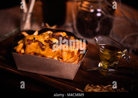 Pommes essen Foto. Street Food. Ungesunde lecker Gegrilltes, Pommes Frites mit Käse und Speck in hausgemachten Handwerk. Mit unscharfen Hintergrund Nahaufnahme. Ru Stockfoto