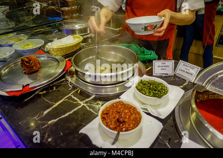 Singapur, Singapur - Januar 30. 2018: In der Nähe von Frau s Hand mit einem riesigen metallenen Löffel die Penang asam laksa Reis Nudeln innerhalb der weißen Schale mit Würziger Fisch tamarind Suppe und frischen Kräutern servieren in Singapur Stockfoto