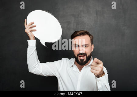 Schließen Sie herauf Foto der Überzeugten strengen Mann mit leeren Sprechblasen und zeigen Sie mit dem Zeigefinger an der Kamera über dunkle graue Wand Platz kopieren Stockfoto