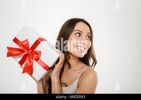 Nahaufnahme Foto von erfreut kaukasische Frau zur Seite schauen beim zeigen Geschenkbox mit roter Schleife auf Kamera isoliert auf weißem Hintergrund Stockfoto