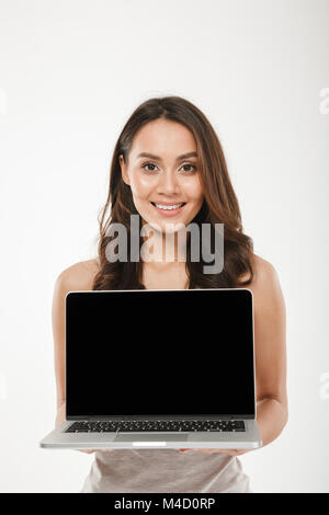 Vertikale Bild der erwachsenen Frau 30er lächelnd und schwarzen leeren Bildschirm von Silber Laptop auf Kamera über weiße Wand Stockfoto