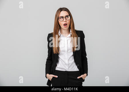 Porträt einer Entsetzte Geschäftsfrau in Anzug gekleidet stehen, blickte isoliert über grauer Hintergrund Stockfoto