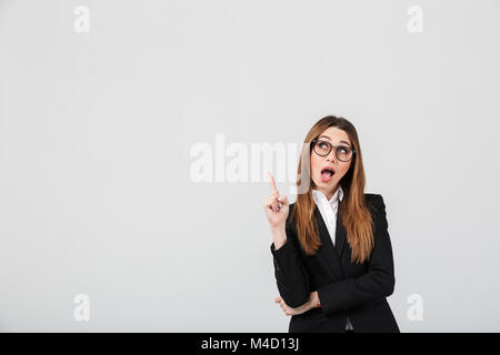 Portrait einer aufgeregt Geschäftsfrau in Anzug gekleidet stehen und zeigen mit dem Finger auf isolierte über grauer Hintergrund Stockfoto