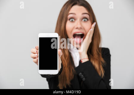 Glücklich überrascht businesslady zeigt Smartphone mit leerer Bildschirm, während Sie die Kamera isoliert Stockfoto