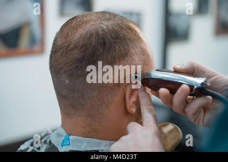 Mann bekommt einen coolen Haarschnitt im barbershop. Friseur schneidet Maschine. Stockfoto