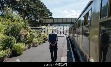 Zugbegleiter wartet als Reisende steigen und ein Erbe Dampfzug bei Winchcombe Station, Gloucesterhire verbinden. UK. Stockfoto