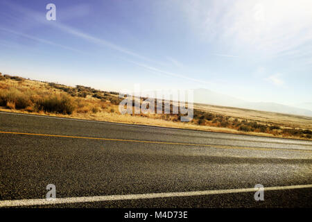 Eine abgewinkelte Straße in der Wüste von Utah mit Cirrus Wolken, hoch in den Himmel. Stockfoto