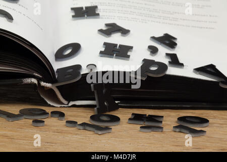Schwarze Buchstaben fallen heraus aus dem Buch auf der Eiche Tisch als Symbol für den Verlust von Wissen in der digitalen Welt. Stockfoto