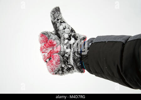 Eine rote behandschuhte Hand, die einen Daumen nach oben in den Schnee. Stockfoto